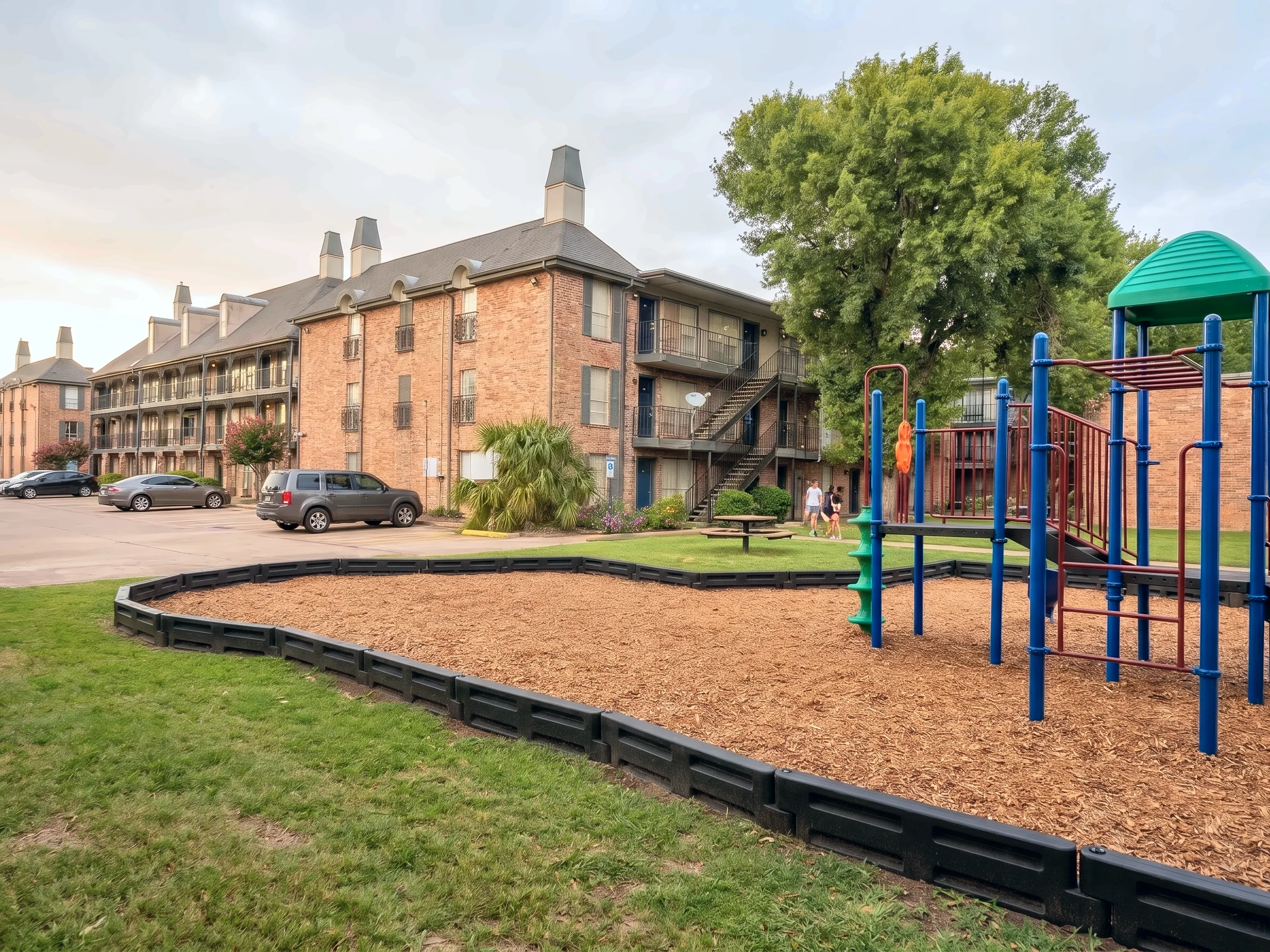 Área de juegos para niños sobre el césped, con edificios de ladrillo detrás